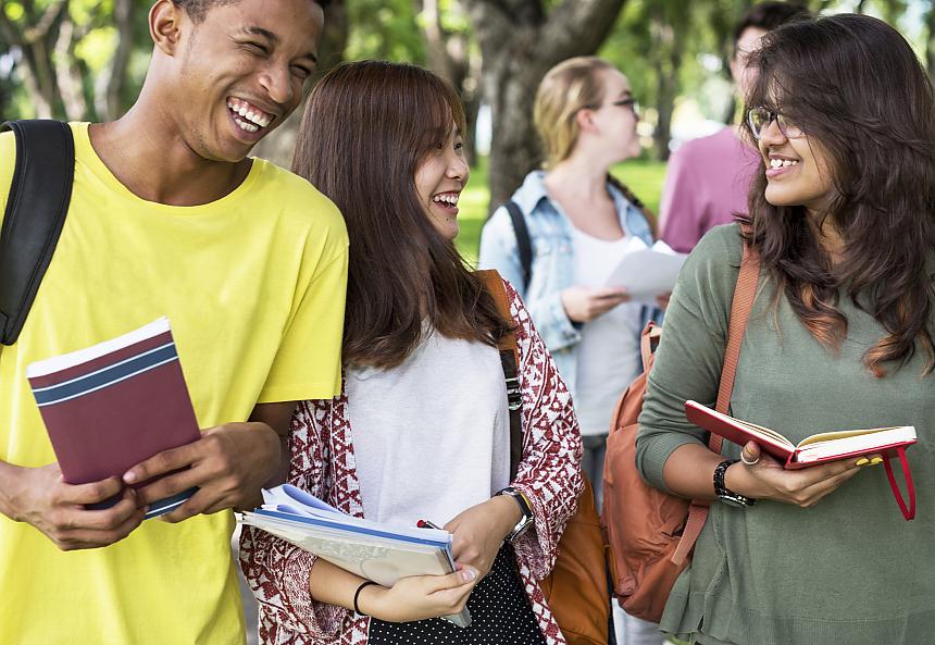 Three college students smiling carrying notebooks.