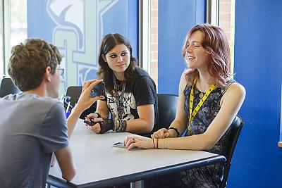 Three students sitting in the dining hall having a conversation. 